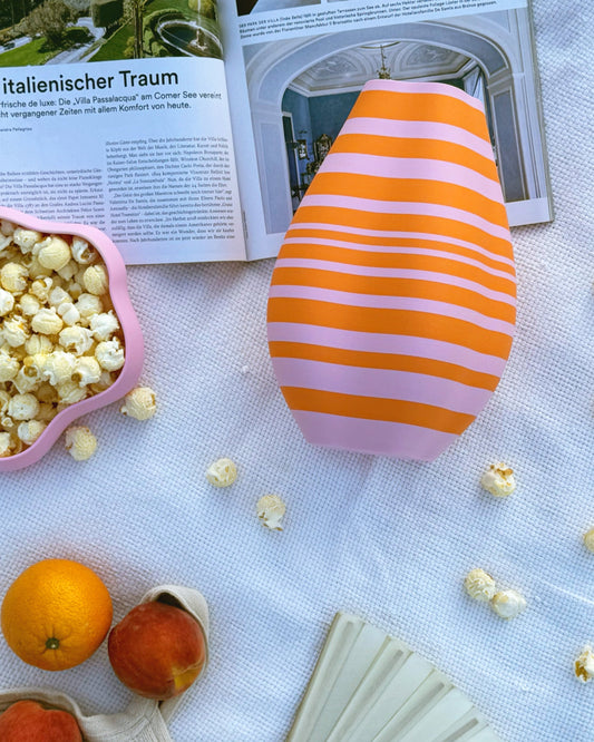 3D-gedruckte Vase in Orange und Pink mit ungleichmäßigem Streifenmuster, Designer Piece, auf einer weisen Picknickdecke, 